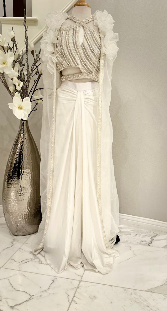 Beautifully crafted 3 piece shrug set in pure silk with pearl embellishment on the asymmetrical crop-top. Paired with long open shrug  in soft organza with pearl lace on the open edges. Paired with a plain white pleated front skirt

Size available 38 with margin.