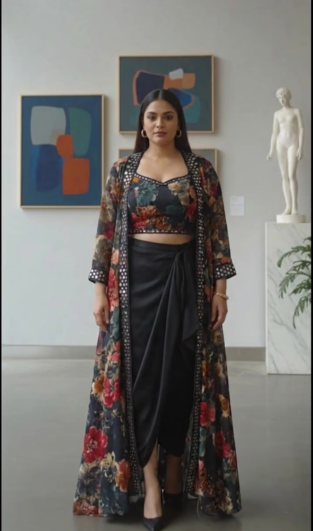 Woman in a floral indo western outfit standing in an art gallery with paintings and sculptures in the background.